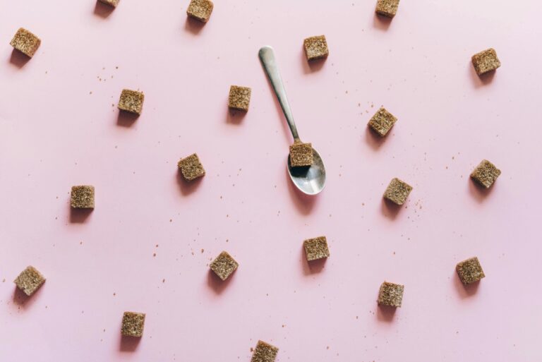 Top view of brown sugar cubes scattered on a pink background with a spoon.